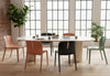 Six Emi Stackable Office Seating chairs in morandi green, coral and black arranged around a large marble collaboration table in an office setting with exposed brick walls, wooden flooring, tall windows and greenery, showcasing modern stackable workspace seating.