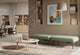 Two Omni Upholstered Office Benches are arranged on a patterned rug, creating a flexible touchdown point in a modern open-plan office. Each green upholstered bench, made with durable 100% polyester OTE fabric, features a built-in plug socket for convenient device charging of laptops and mobile devices. A round coffee table with a laptop completes this inviting collaborative zone, designed for flexible working, informal meetings and casual collaboration.