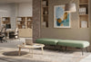Two Omni Upholstered Office Benches are arranged on a patterned rug, creating a flexible touchdown point in a modern open-plan office. Each green upholstered bench, made with durable 100% polyester OTE fabric, features a built-in plug socket for convenient device charging of laptops and mobile devices. A round coffee table with a laptop completes this inviting collaborative zone, designed for flexible working, informal meetings and casual collaboration.