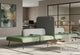 The Omni Acoustic Bench System, a versatile seating solution, features two dusty teal upholstered benches and a central dark grey acoustic privacy divider in a modern open-plan office. Integrated wooden side tables with power outlets and a hook on the divider enhance functionality. This modern office furniture provides acoustic comfort and flexible workspace design for focused work or informal collaboration, promoting productivity and employee wellbeing.