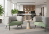 Two Omni Curved Arm Lounge Chairs are positioned facing each other across a small, modern round table in a bright, open-plan office environment. Each lounge chair, featuring a sculptural silhouette with gently contoured pebble grey backrests and dusty teal seats upholstered in polyester OTE fabric. The setup creates an inviting collaborative workspace or breakout space for informal meetings or focused individual work