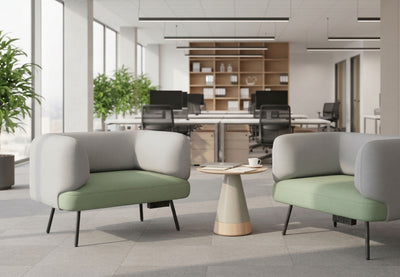 Two Omni Curved Arm Lounge Chairs are positioned facing each other across a small, modern round table in a bright, open-plan office environment. Each lounge chair, featuring a sculptural silhouette with gently contoured pebble grey backrests and dusty teal seats upholstered in polyester OTE fabric. The setup creates an inviting collaborative workspace or breakout space for informal meetings or focused individual work